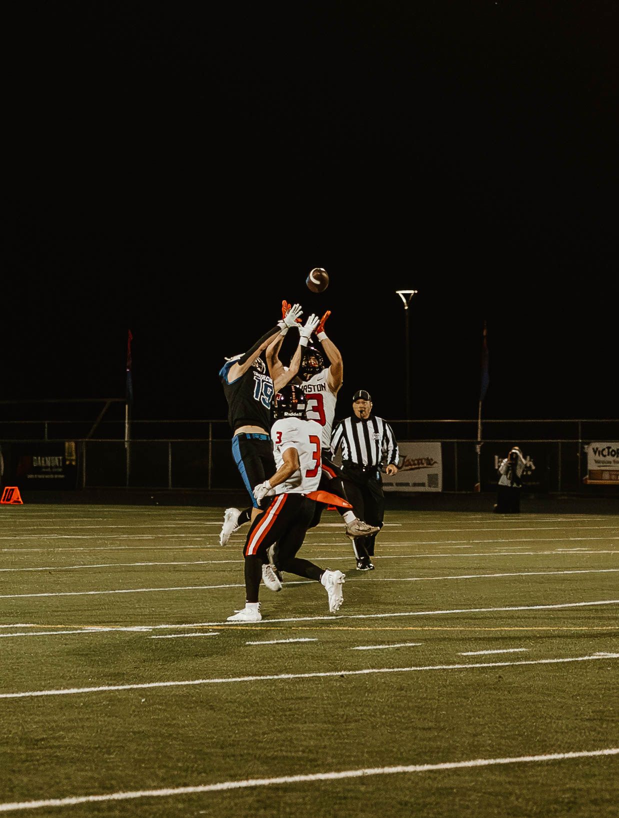 Athletes compete in an intense play during a nighttime football game on an illuminated field.