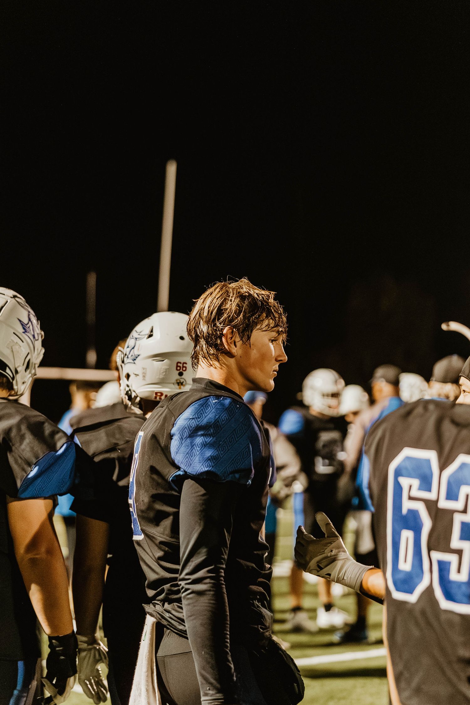 Football players in black uniforms line up on a nighttime field during a game.
