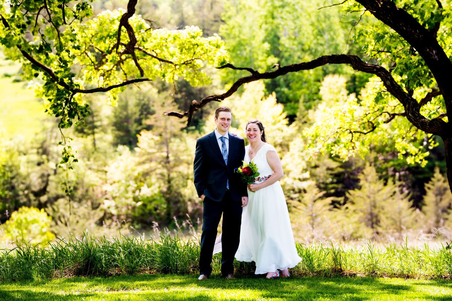 A couple shares a romantic moment under sunlit trees in a lush garden setting during their wedding celebration.