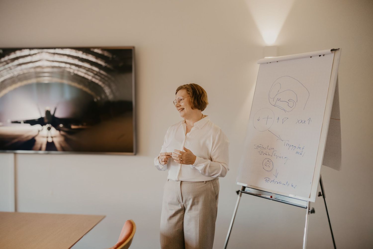 A presenter stands next to a flipchart during a business presentation in a modern conference room.