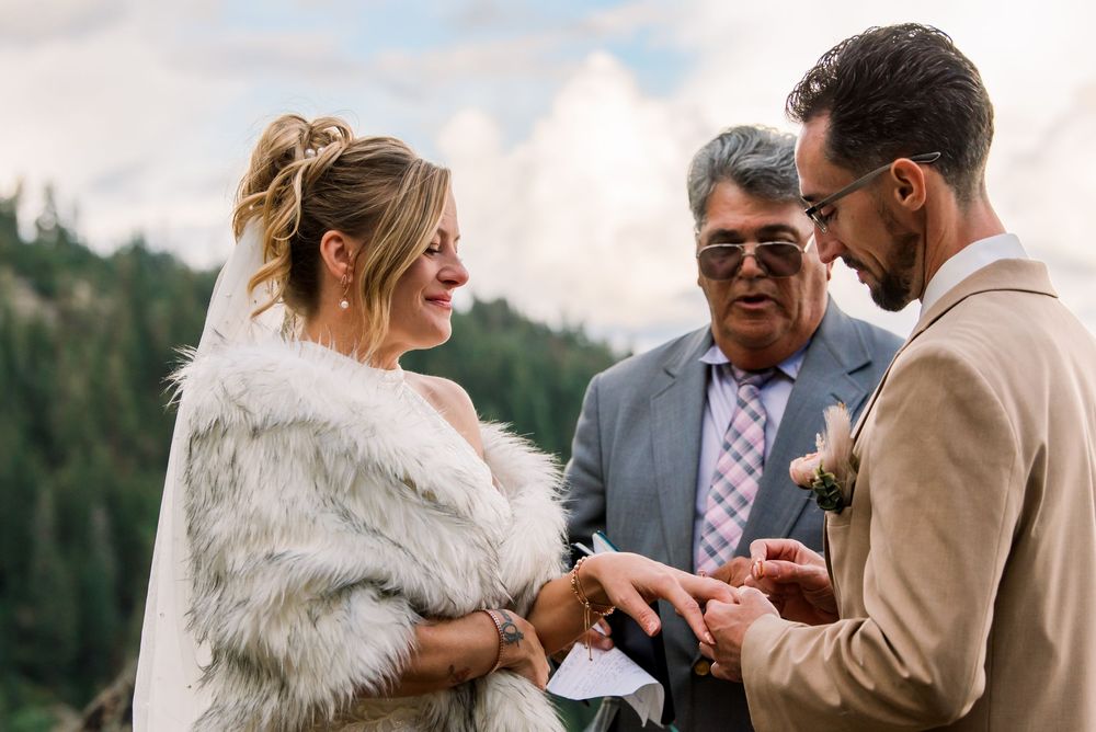 A couple shares an intimate moment during their wedding ceremony in a scenic outdoor mountain setting.