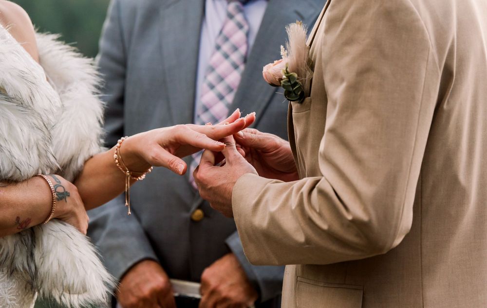 Close-up of hands during wedding ring exchange ceremony with officiant in background.