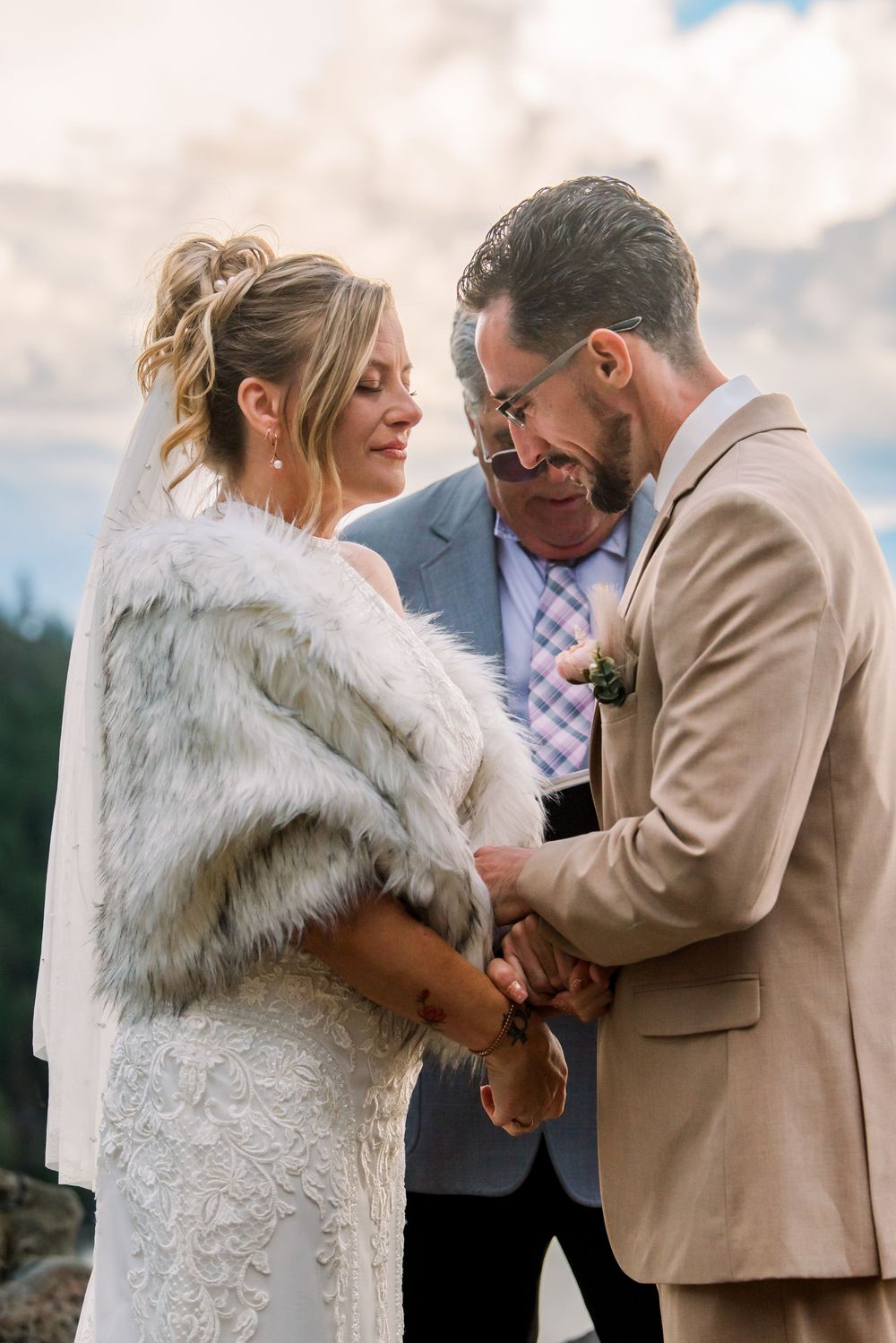 A romantic wedding ceremony moment as a couple exchanges rings outdoors on a cloudy day.