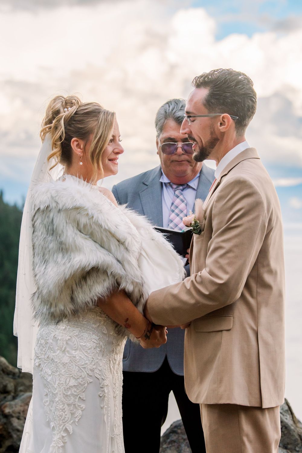 Wedding ceremony taking place outdoors with couple embracing in white dress and tan suit.