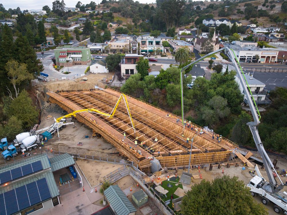 A street bridge is under construction as two cranes pour concrete into the road.