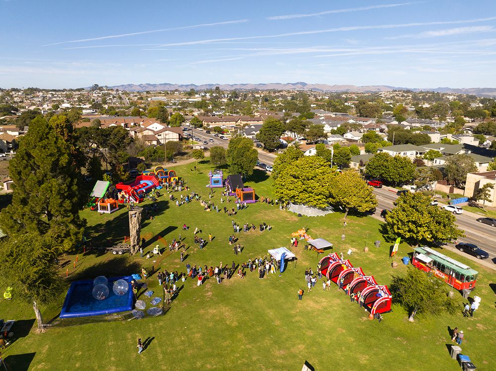 Aerial view of a Halloween event at a park in Arroyo Grande. There are people and lots of inflatable games and bounce houses.