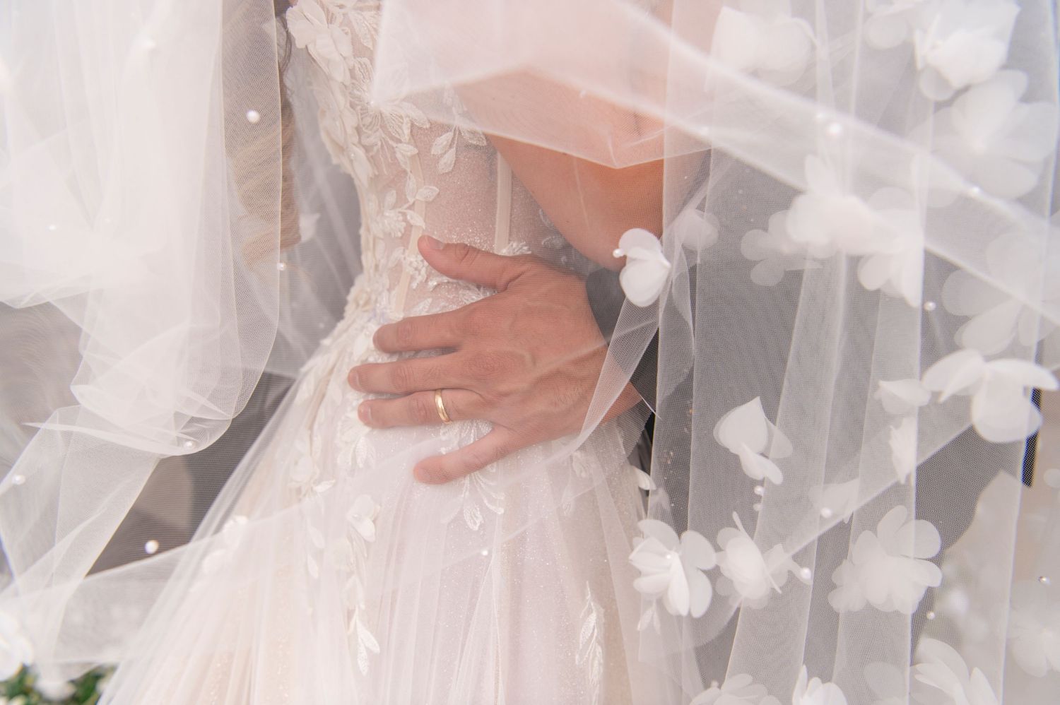 Close-up detail of a white wedding dress with delicate tulle overlay and small floral appliques.