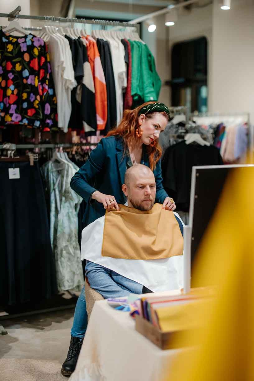 Retail workers collaborating at a clothing store counter with racks of colorful garments visible in the background.