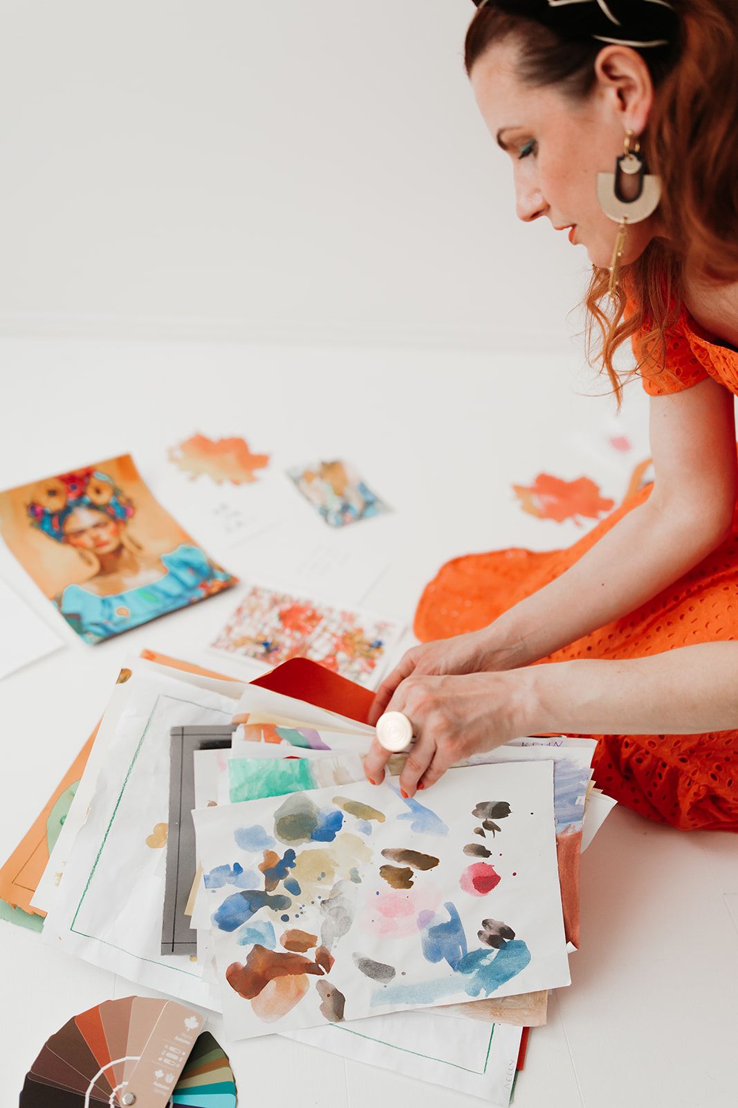 Artist works on watercolor fashion illustrations at white desk with colorful paint swatches and sketches.