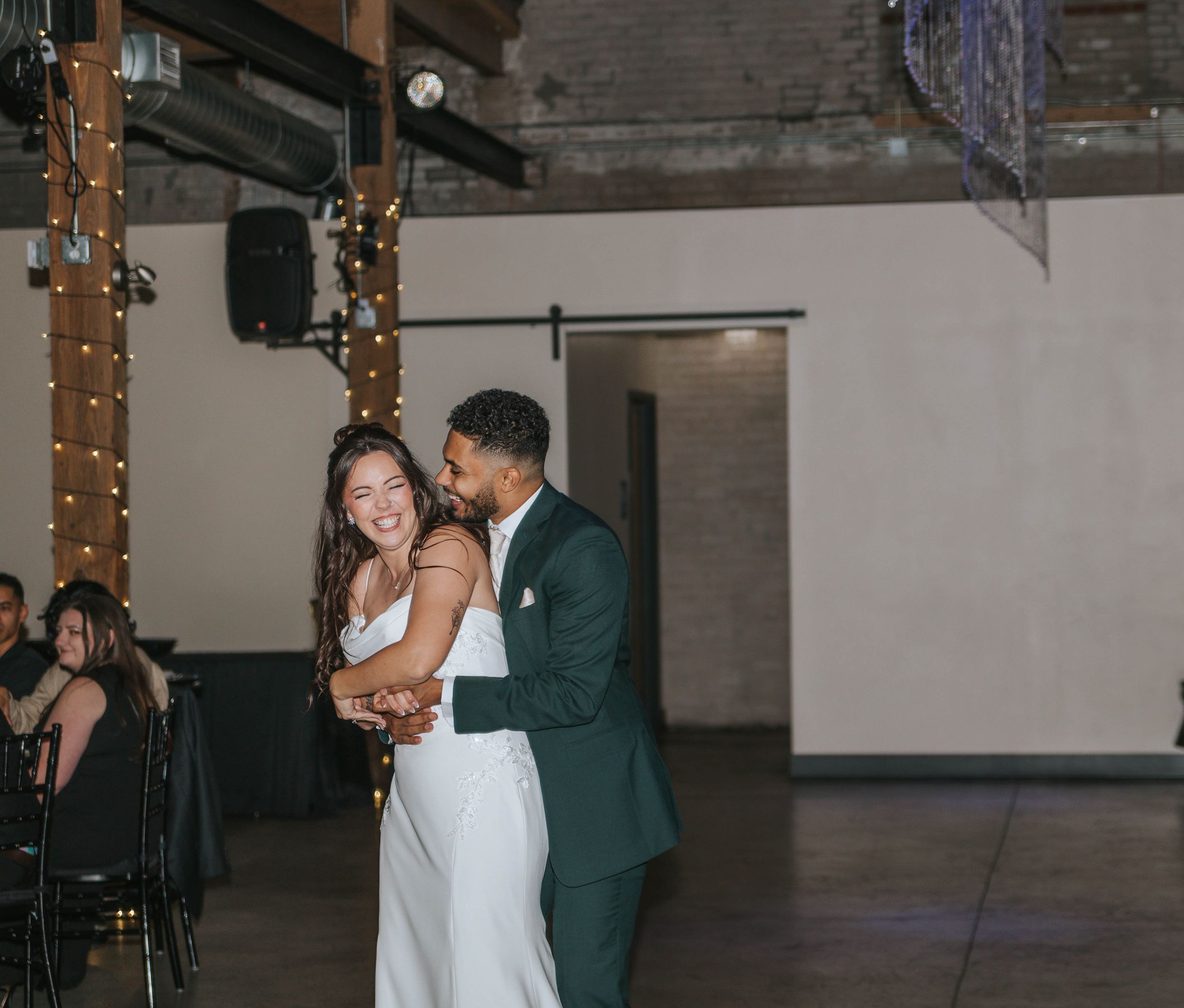 Wedding couple dancing together in a rustic industrial venue decorated with string lights.