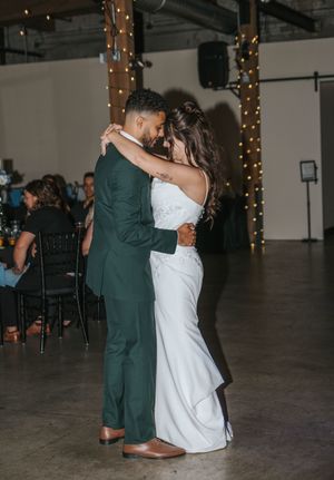 Newlywed couple shares their first dance at wedding reception with romantic string lights in background.