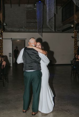 A couple in formal attire sharing a slow dance at an event in a dimly lit venue.