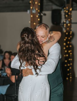 A couple shares an intimate dance moment at a wedding reception with twinkling lights in the background.
