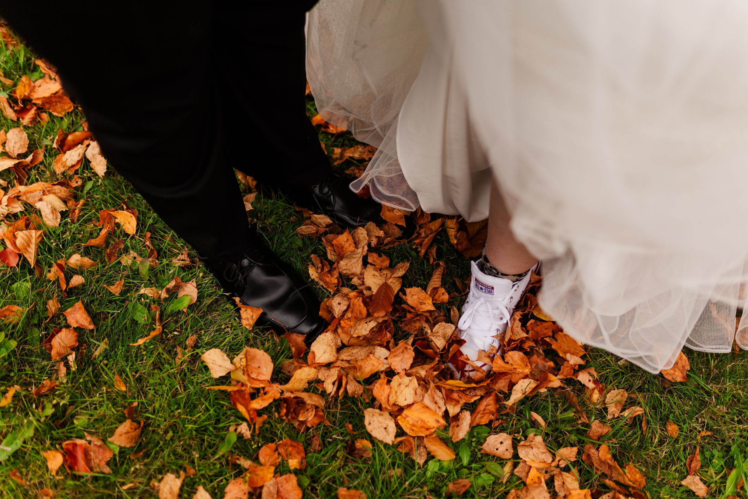 Fallen autumn leaves scattered on grass with a flowing white dress in the corner of the frame.
