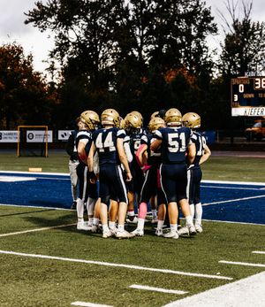 Football team huddles together on field during night game wearing blue and white uniforms.