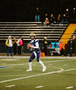 A football player in a navy uniform stretches on the field during a game or practice session.