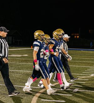 Football players in navy and gold uniforms line up in formation on the field.
