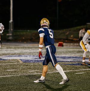 Football player in navy uniform performs quick footwork drills on artificial turf field during practice session.