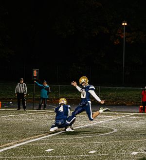 Football player in navy and gold uniform slides across the field during a night game.