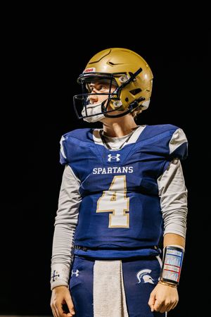 Football player in blue Spartans jersey #4 with gold helmet stands ready on dark field.