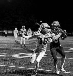 Two football players in opposing uniforms compete for the ball during a nighttime game on the field.