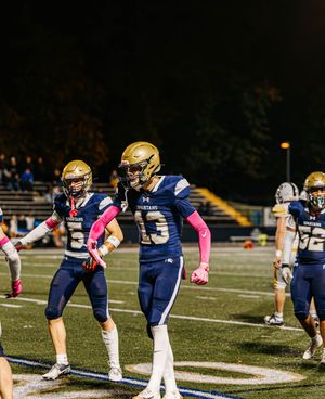 Football players stretch in formation on blue turf field wearing navy uniforms with pink accessories.