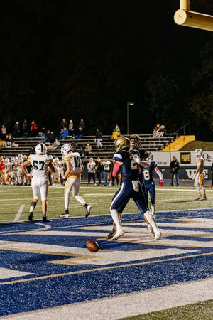 Football players from opposing teams face off in the endzone during a night game.