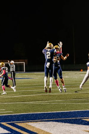 Football players in navy and pink uniforms line up in formation on an illuminated field during a nighttime game.