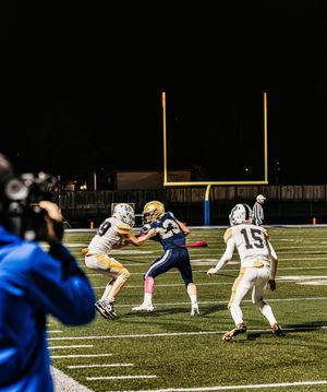 Football players execute a field goal attempt during a nighttime game on an illuminated field.