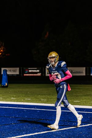 Player in navy uniform with gold helmet runs across blue end zone during night game.