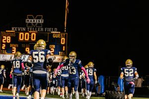 Football players gather on the field at night with illuminated scoreboard showing time remaining.