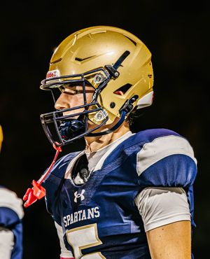 Spartans football player in gold helmet and navy uniform stands focused during game.