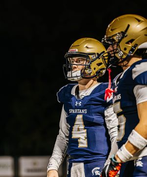 Football players in blue uniforms and gold helmets stand together during night game.