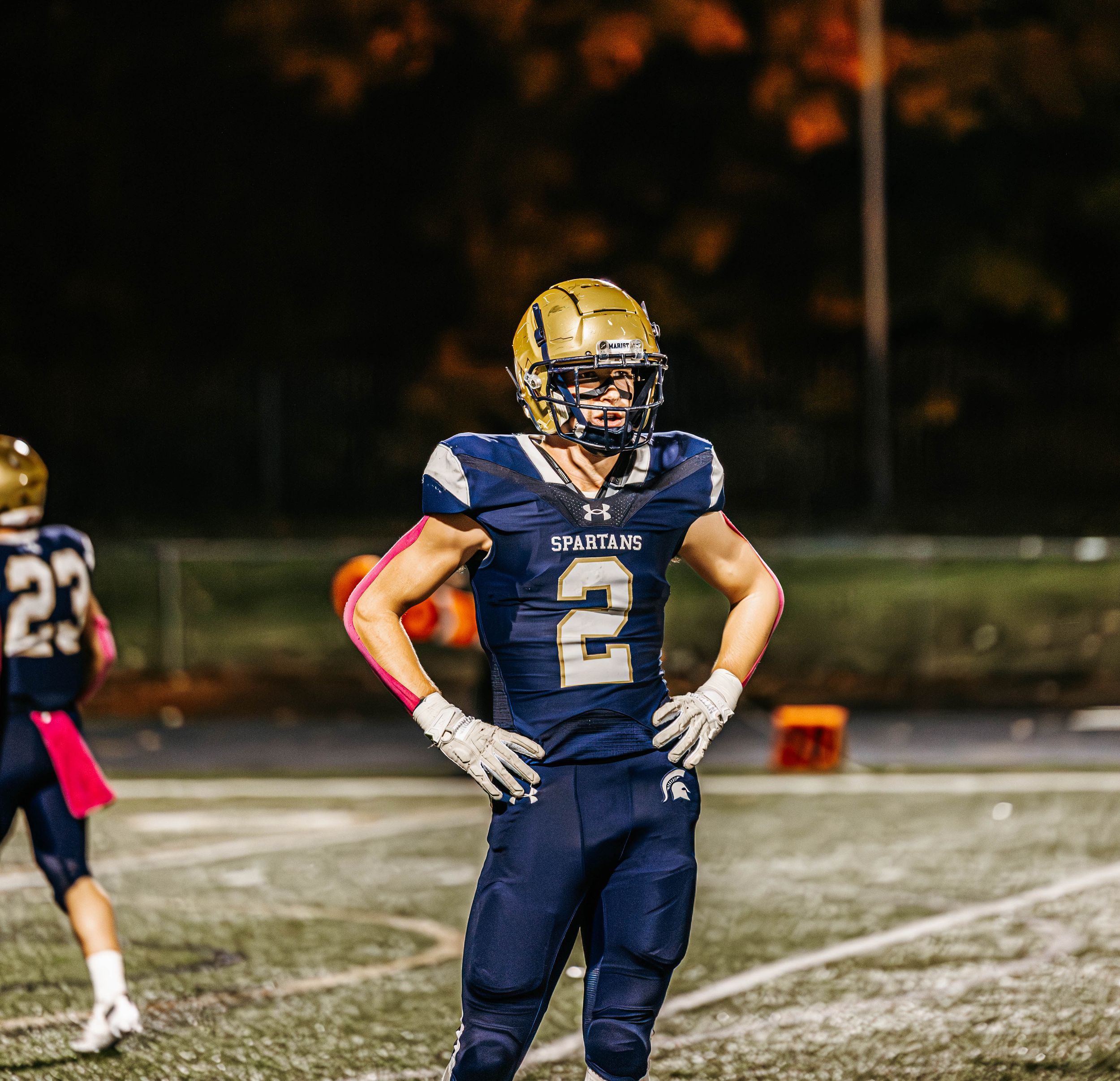 Football player in navy and gold uniform stands ready on snowy field during night game.