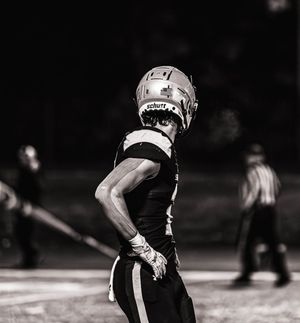 Black and white photo of football players in motion during nighttime game.
