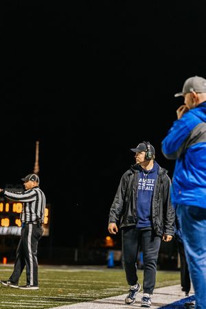 Football referees gather on a dark field at night under stadium lights during a game.
