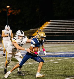 Football players in navy and gold uniforms compete on an illuminated field at night.