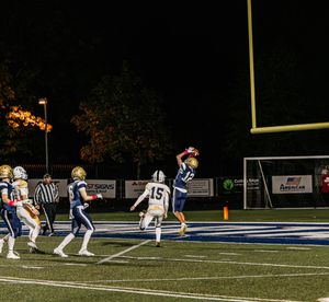 Football players line up on the field during a nighttime game with stadium lights illuminating the artificial turf.