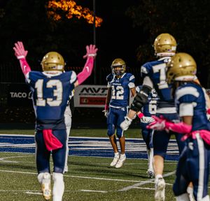 Football players in blue uniforms with pink accessories spread across field during night game.