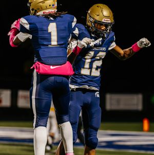 Two Spartans football players in blue uniforms celebrate together on the field.