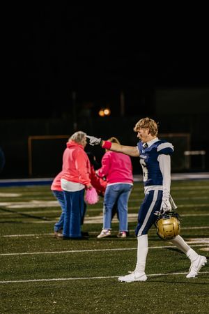 Football players stretch and warm up on a dark field at night with some wearing pink and navy uniforms.