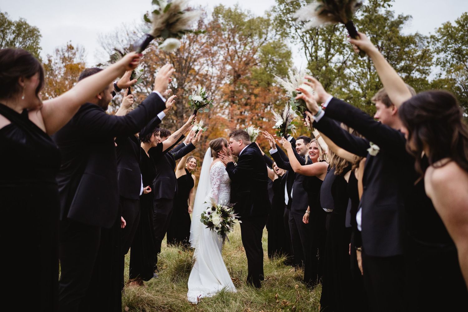 Wedding party celebrates by tossing autumn leaves into the air during outdoor celebration.