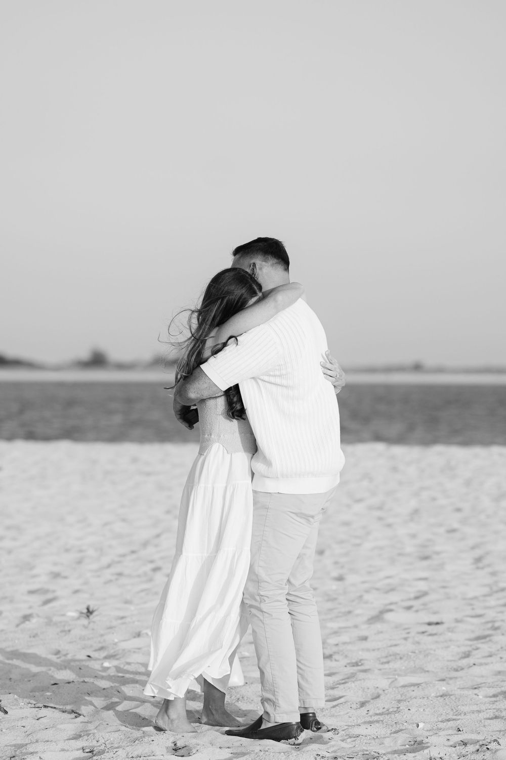 Black and white photos capture a couple's emotional embrace on a sandy beach after they get engaged.