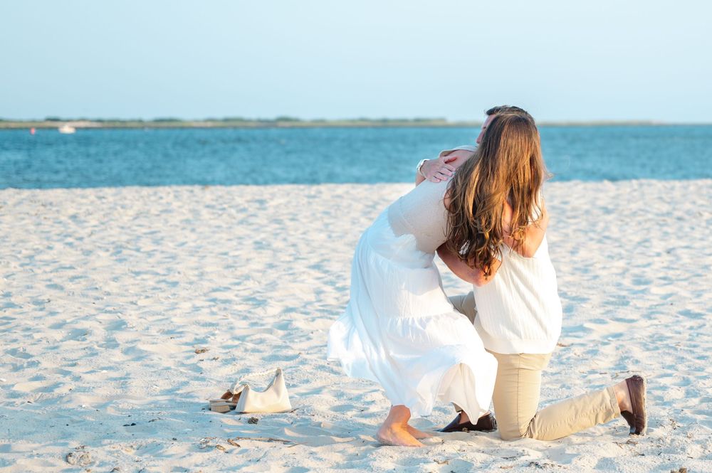 A couple in white outfits relaxes on a pristine beach with turquoise water and soft sand in the background.
