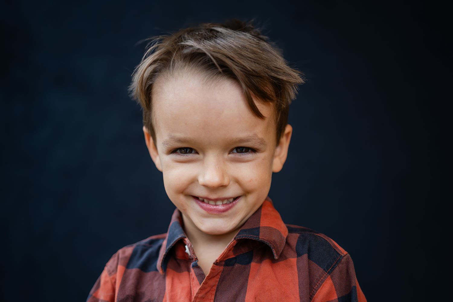big smiles for a school portrait of a young boy with red and black plaid shirt