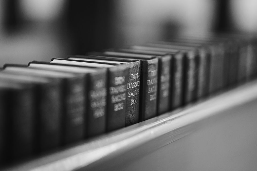 Monochromatic view of book spines lined up on a shelf with shallow depth of field effect.