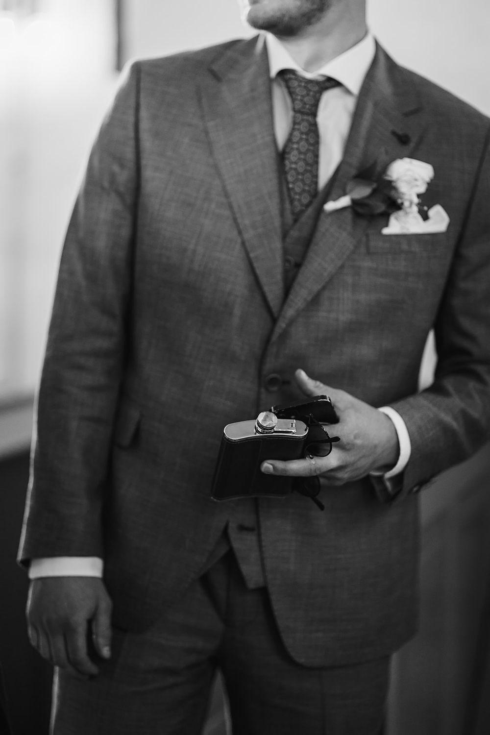 Men in gray suits holding up cufflinks in a black and white wedding preparation photo.