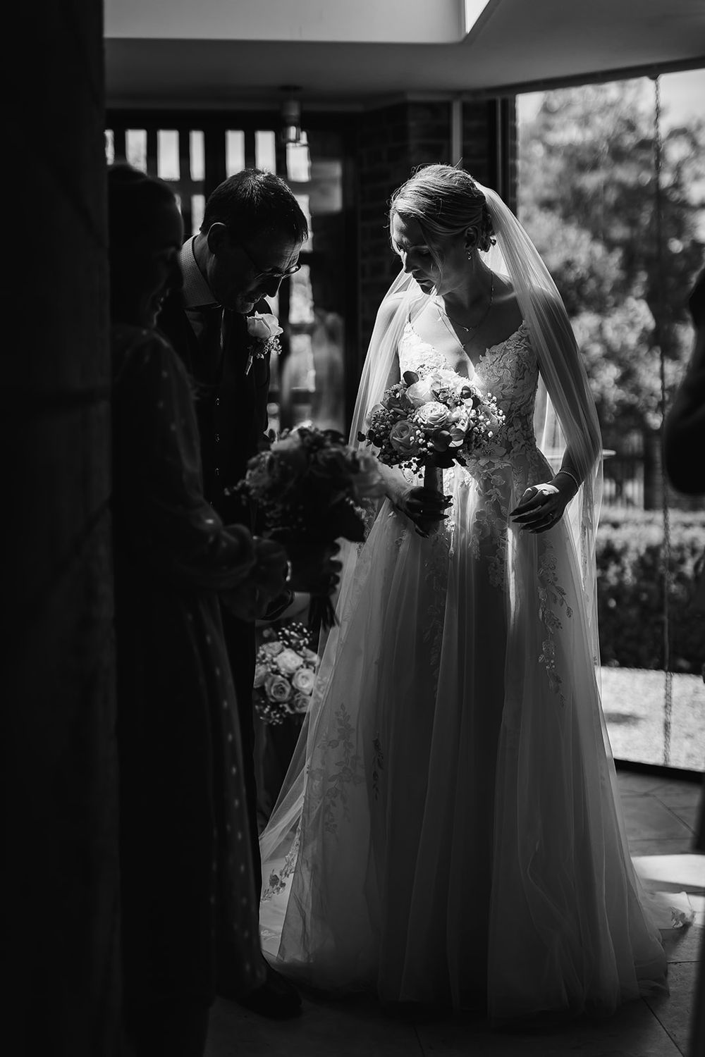 A group of bridesmaids in white flowing dresses stand together in a black and white wedding photograph.