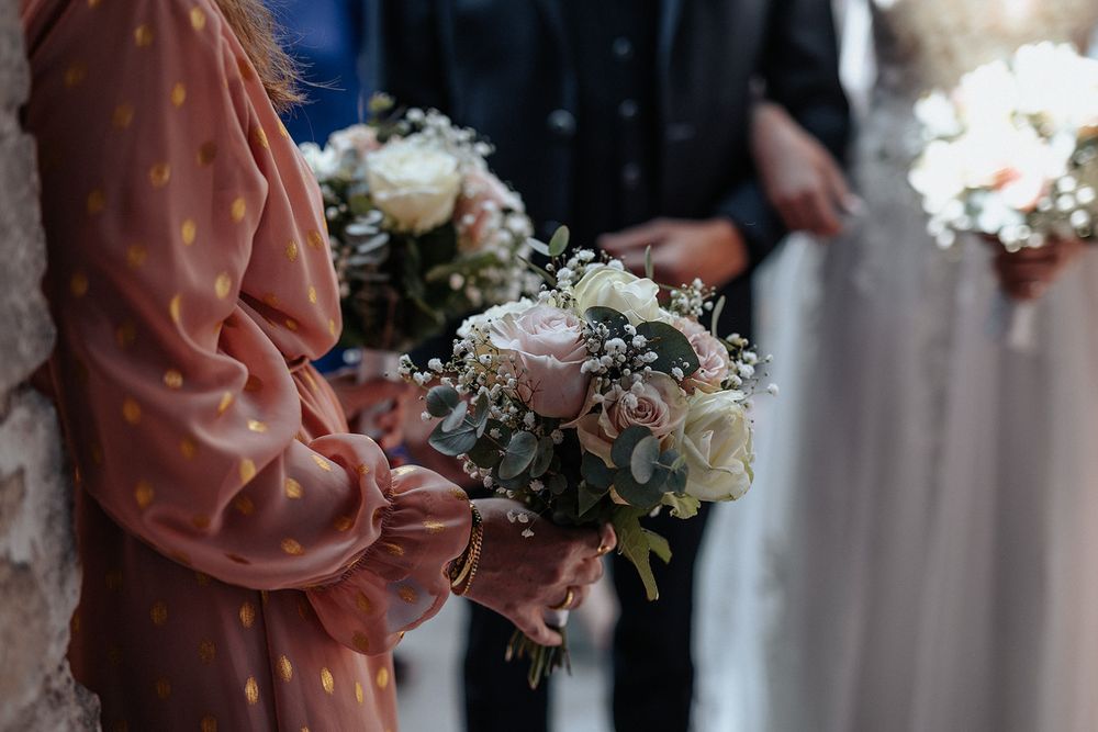 Wedding party members hold elegant bouquets with white roses and greenery against formal attire at ceremony.