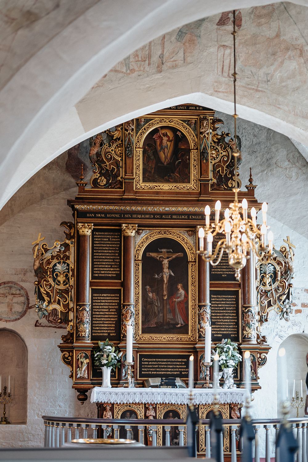 Ornate baroque church memorial plaques with gold details and chandeliers mounted on white stone walls.